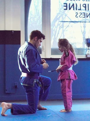 BJJ instructor working with a little girl in a pink gi