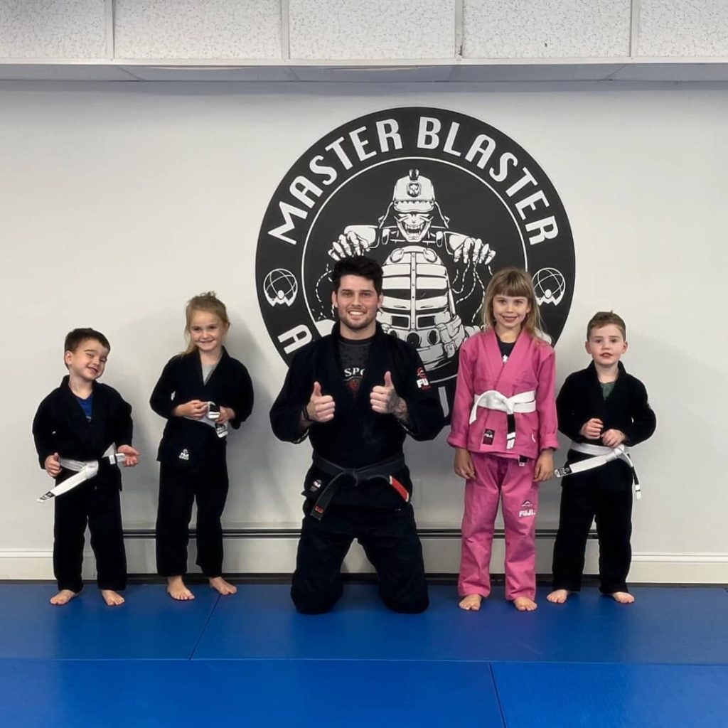 children pose with their jiu jitsu instructor in Atlas Jiu Jitsu's Waltham, MA gym